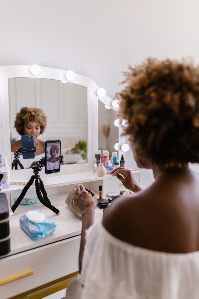 Services A woman engaged in vlogging in front of a lit vanity mirror using a smartphone and tripod.